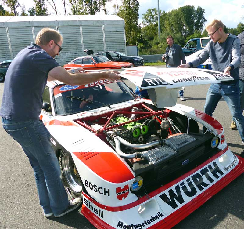 Gemeinschaftliches Arbeiten: Für das Foto des Zakspeed-Motors heben Gregor und Lukas Reininger die Haube vom Renner. Rechts im Bild geht das AUTO BILD KLASSIK-Team seiner Arbeit nach: Christian Bittmann fotografiert, Marc Keiterling (rechts) denkt stets über die richtigen Formulierungen nach und Tim Dahlgaard vermisst und wiegt die Autos. Links ist Wolfgang Laufer zu sehen, der „Vater“ der Ford Classic Cars in Köln. Gemeinschaftliches Arbeiten: Für das Foto des Zakspeed-Motors heben Gregor und Lukas Reininger die Haube vom Renner. Rechts im Bild geht das AUTO BILD KLASSIK-Team seiner Arbeit nach: Christian Bittmann fotografiert, Marc Keiterling (rechts) denkt stets über die richtigen Formulierungen nach und Tim Dahlgaard vermisst und wiegt die Autos. Links ist Wolfgang Laufer zu sehen, der „Vater“ der Ford Classic Cars in Köln.