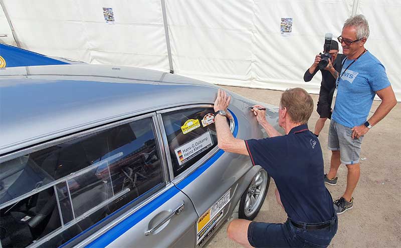 Veredelt: Vor der Abfahrt in Kiel signiert Walter Röhrl den Capri. Günther schaut dem „Rallye-Gott“ dabei genau auf die Finger. Veredelt: Vor der Abfahrt in Kiel signiert Walter Röhrl den Capri. Günther schaut dem „Rallye-Gott“ dabei genau auf die Finger.